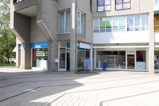 Modernes Geschäftshaus mit großen Fenstern, Arztpraxis und Apotheke im Erdgeschoss.