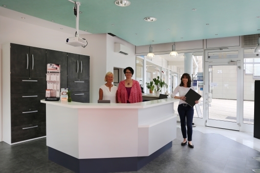 Modernes Empfangsbereich einer Arztpraxis mit drei Mitarbeiterinnen am Tresen.